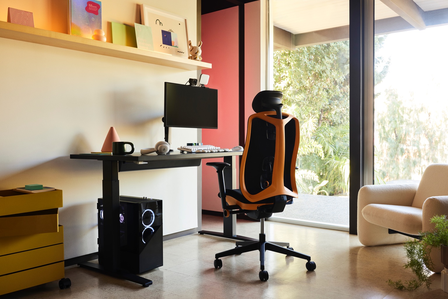 A black Herman Miller gaming chair with orange accents is shown at a desk as part of a residential with a large CPU and monitor. A white lounge chair sits to the right.