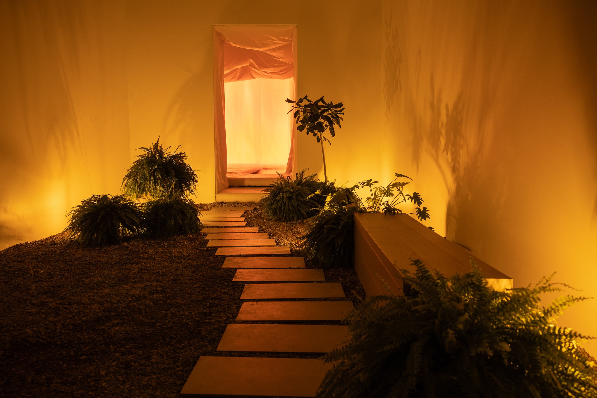 In an installation by Mason Studio as part of the DesignTO festival during Toronto's 2025 design week, a pathway leads to a doorway that looks into a glowing orange room closed off with curtains.