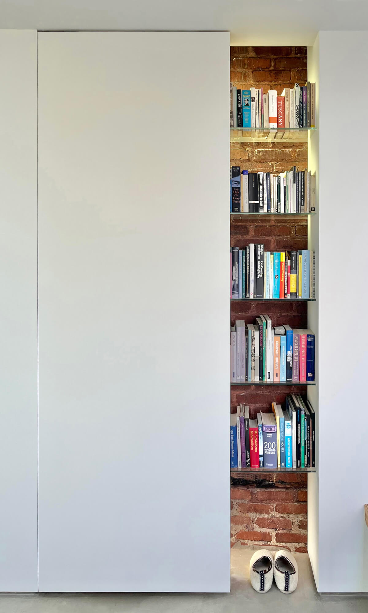 The brick chimney, a vestige of the original structure that reappears in various guises inside and out, peeks through a set of floating bookshelves.