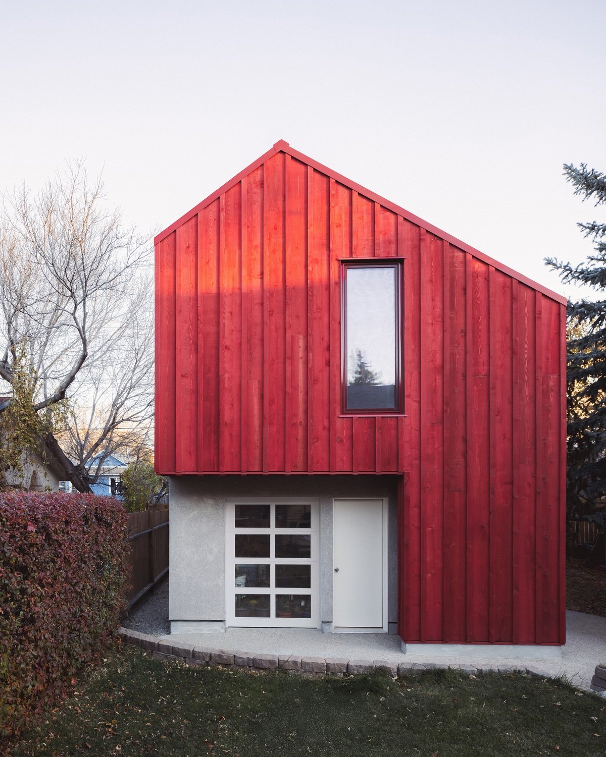 An angular Calgary laneway home by Bold Workshop Architecture featuring angular wood-framed construction cantilevering over a rectangular concrete volume with a roll-up white door.