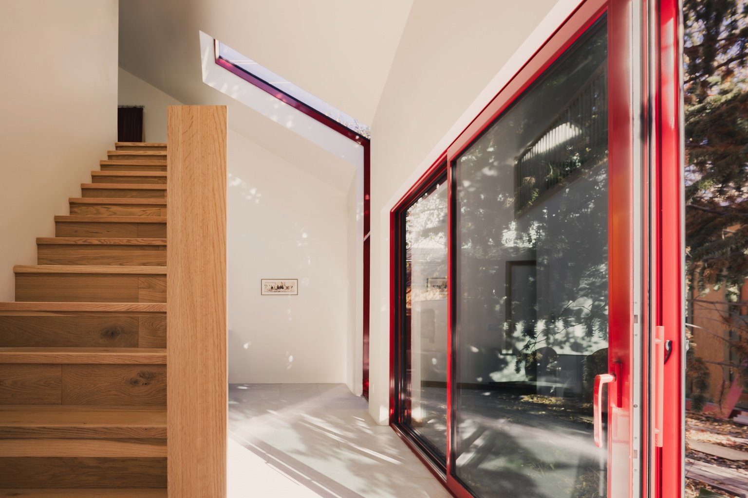 The interior of a Calgary laneway home by Bold Workshop Architecture, with a wooden staircase to the left, a red-framed sliding glass door to the right.