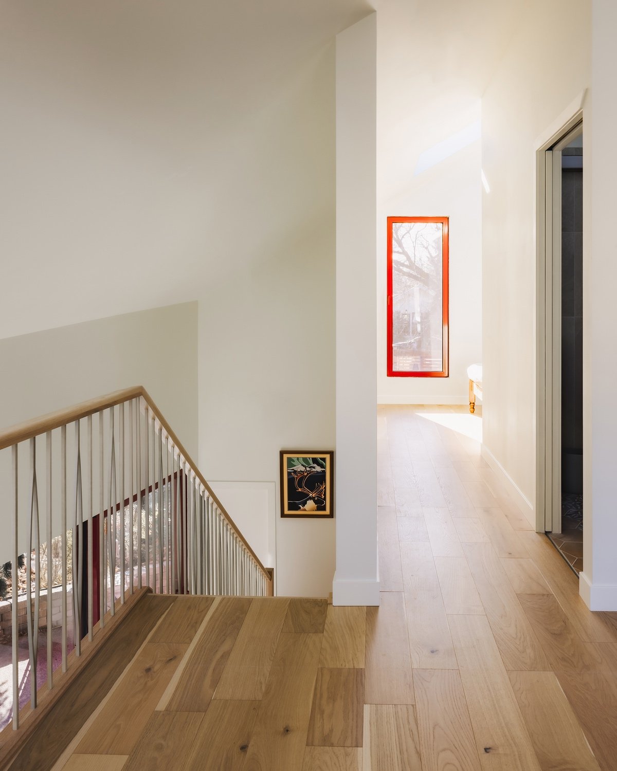 Looking down a hallway to a red-framed window, with a staircase going downstairs to the left.