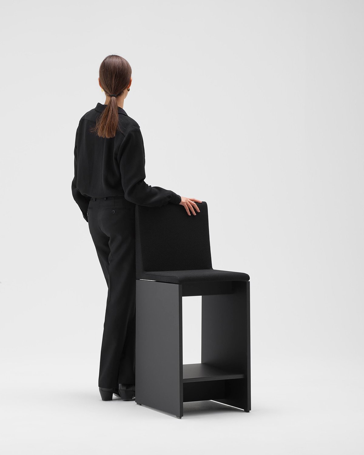 Woman leans against a black stool