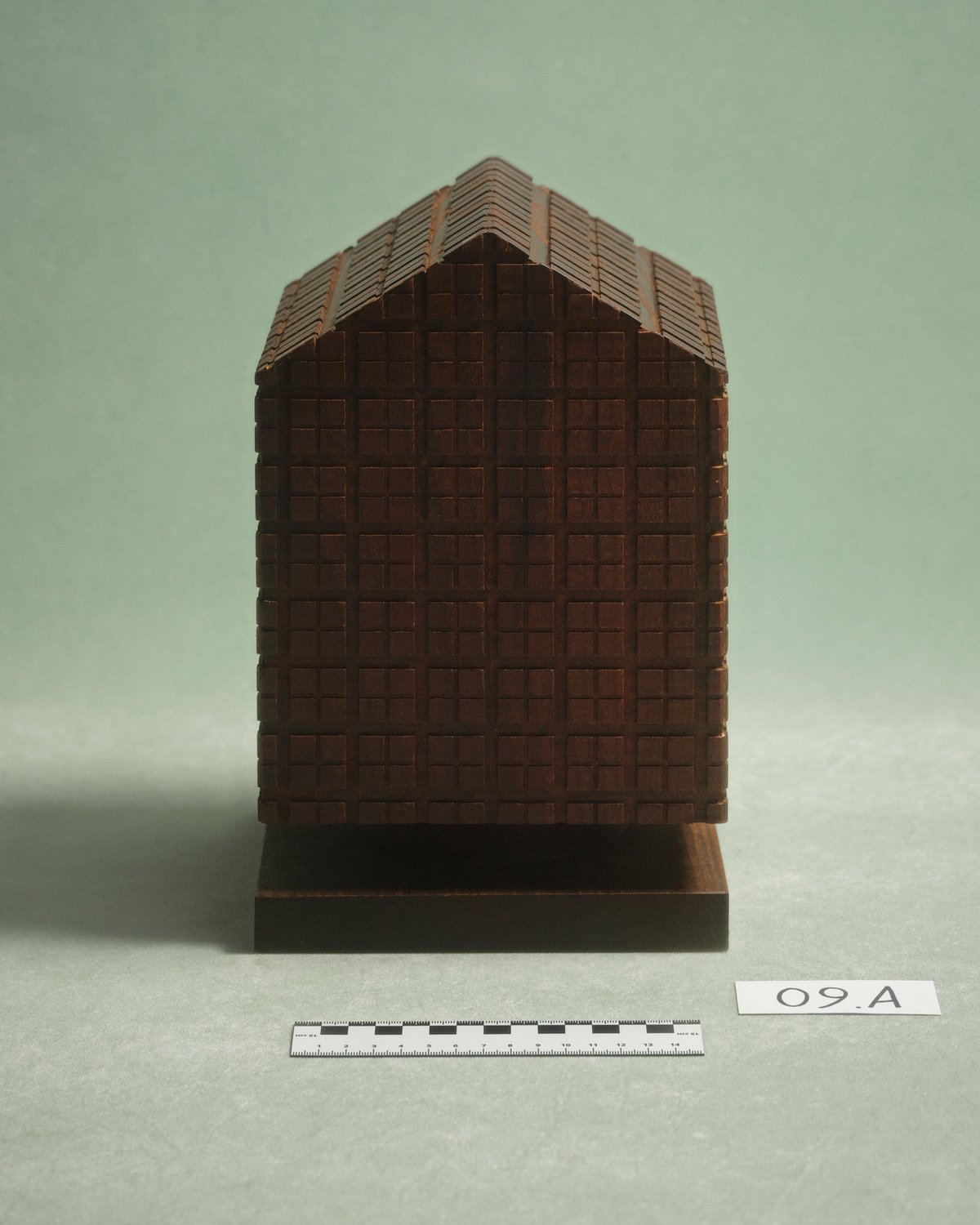 A wooden house sculpture featured in a design typology exhibition of urns organized by Alessi during Milan Design Week 2025.
