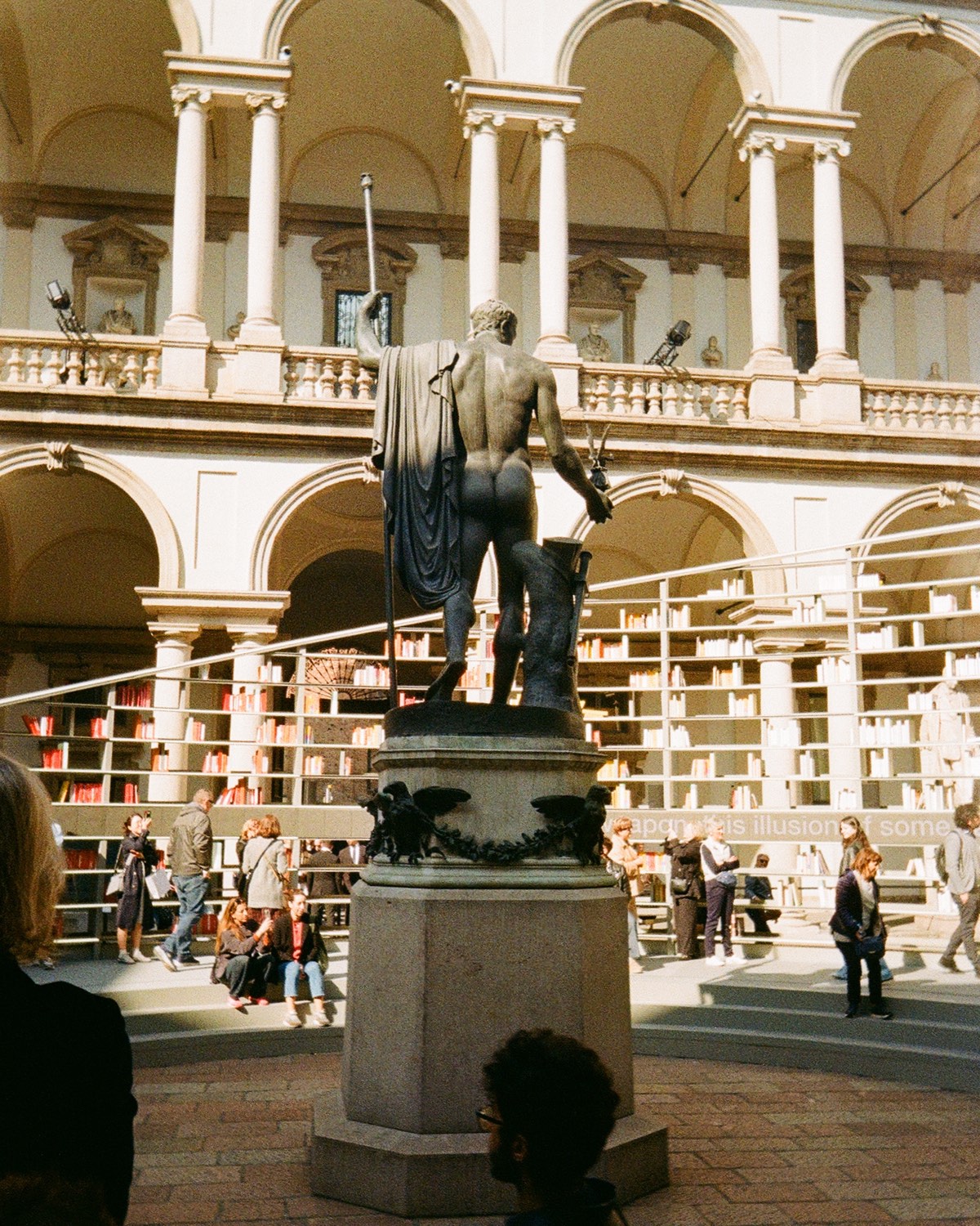 A statue surrounded by a circular bookshelf within a historic courtyard.