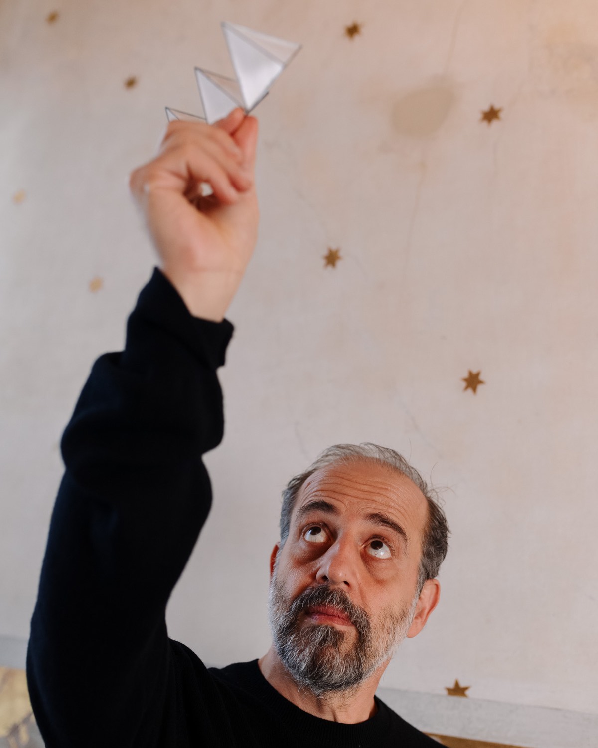 Michael Anastassiades holding a small model of his Cygnet fixture featuring folded paper triangles.