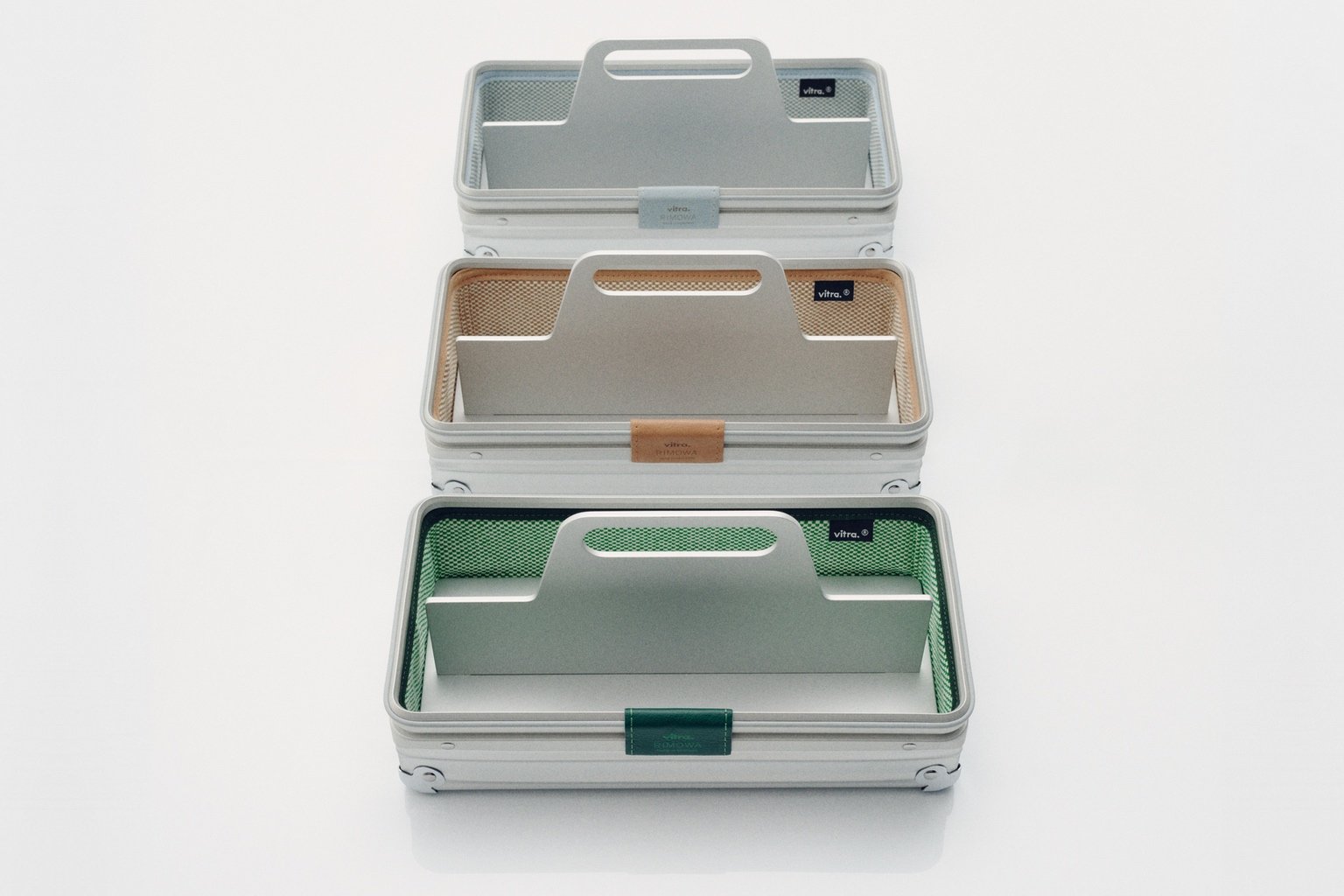 A trio of three grooved aluminum desk caddies, with beige, grey and green upholstered lining.