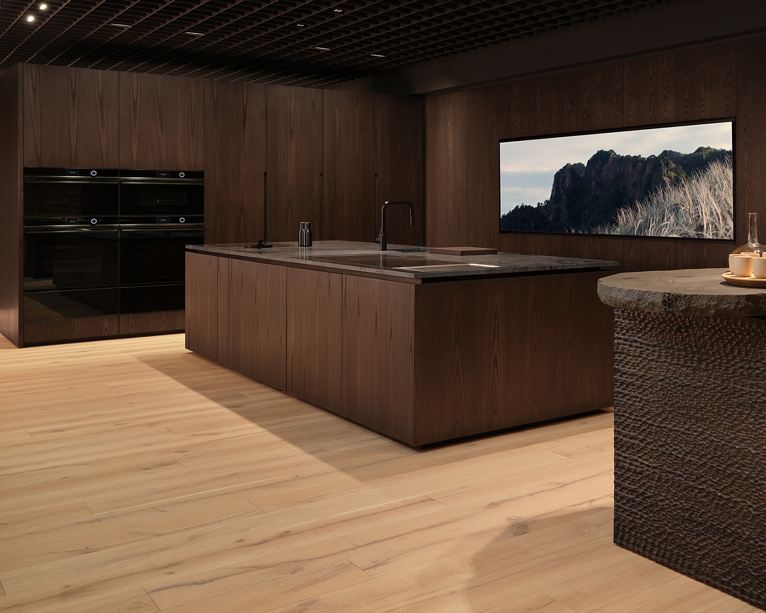 Dimly lit kitchen with dark brown wooden cabinets and island counter in Fisher and Paykel's experience centre