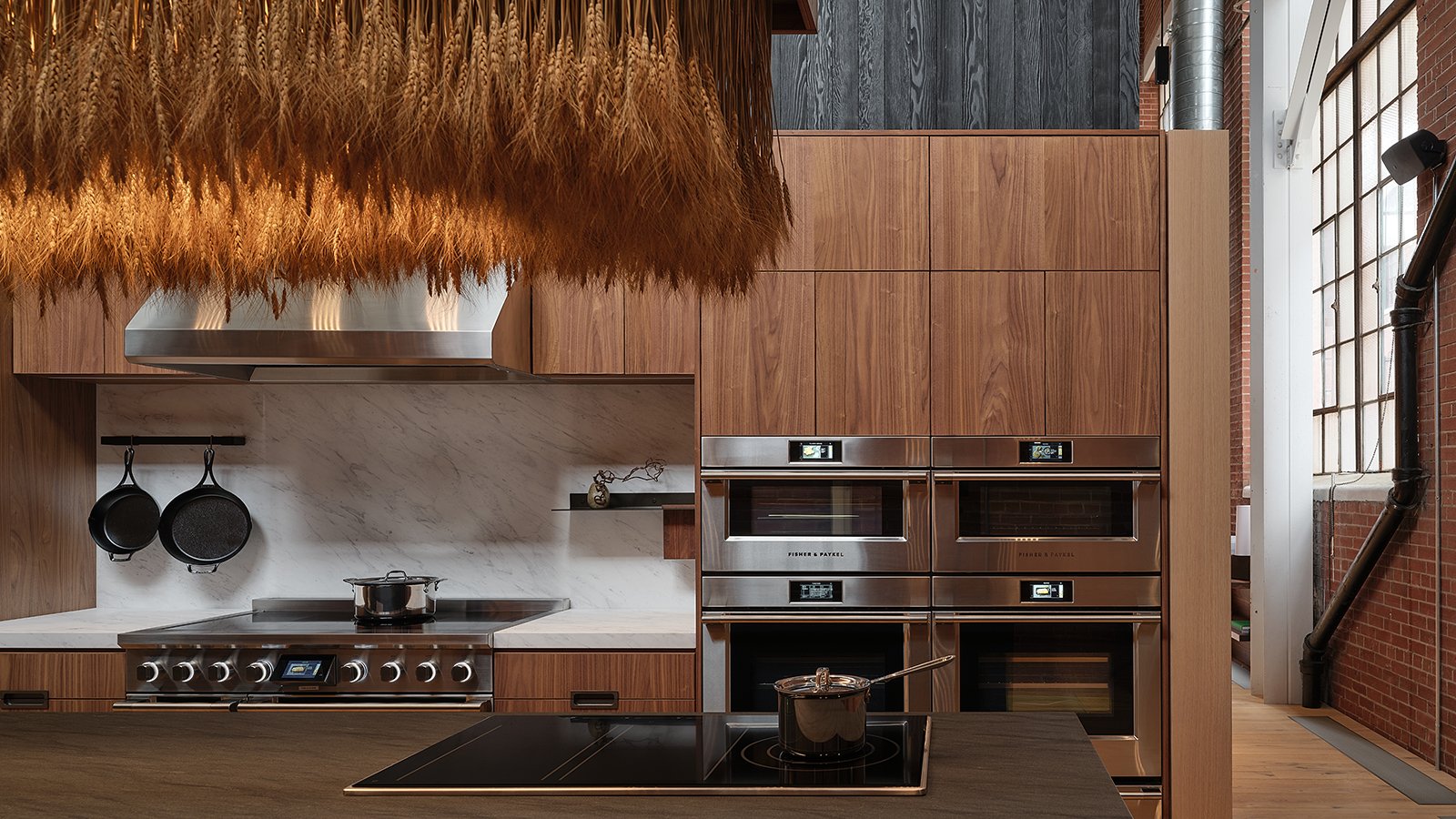 Four stainless-steel ovens, 1 stovetop and brown wooden cabinets with a fringe ceiling light