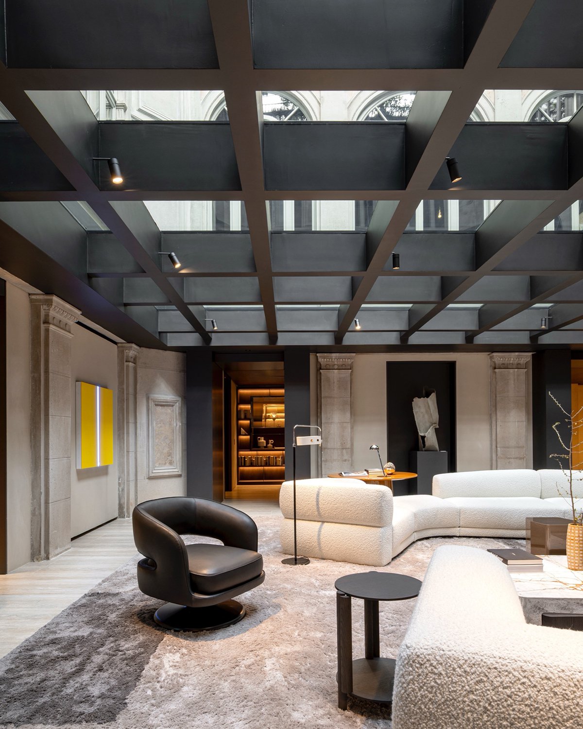 Milan showroom - Internal courtyard at Palazzo Molteni with pilasters and friezes (left), black chair and two white couches under a modern glass ceiling