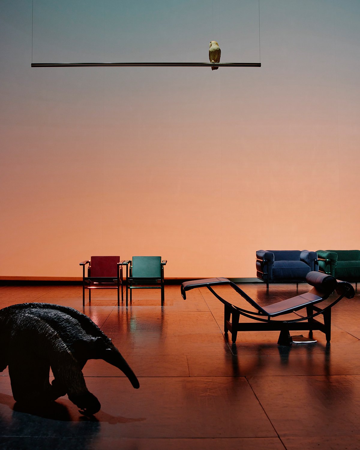 A stage with a sunset background, a bird and animal in the foreground with chairs and sofas in the background