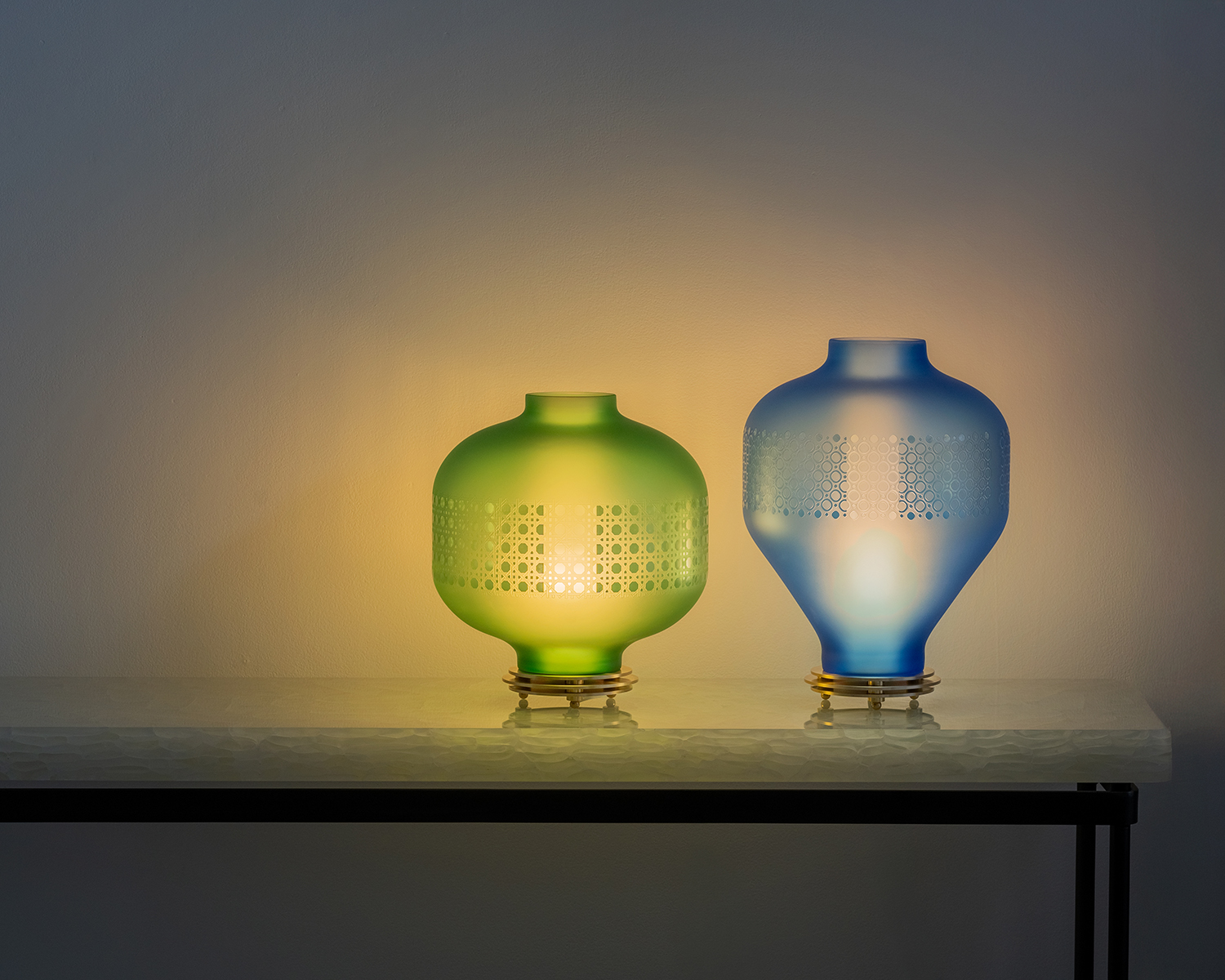 Two lanterns by the goodman studio (green on the left and blue on the right) on a table in a dimly lit room