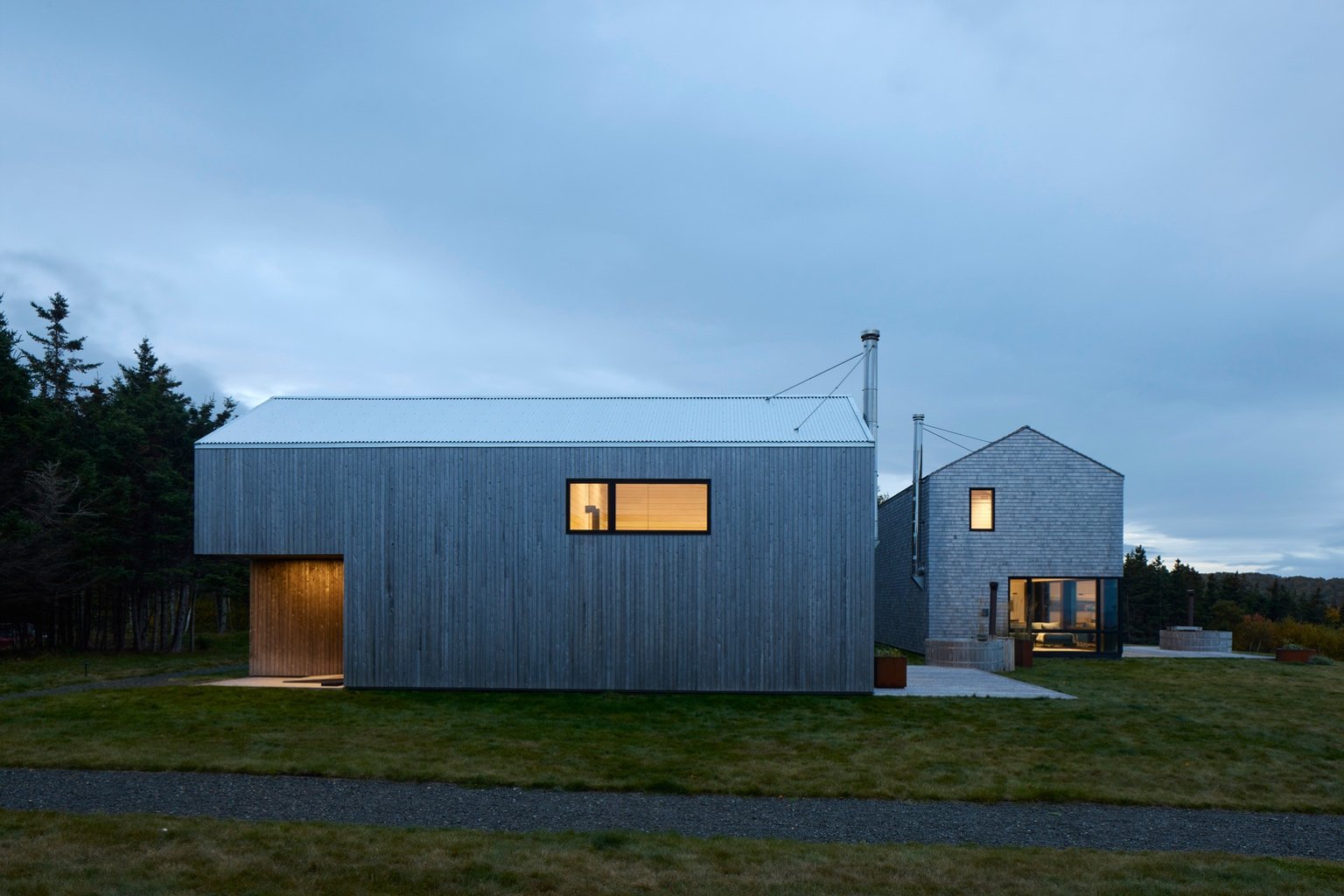 Two coastal modern rental cabins on Cape Breton Island designed by MacKay-Lyons Sweetapple Architects with gabled roofs and grey cedar cladding.