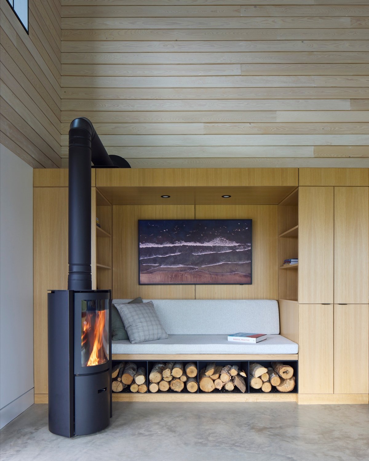 A wood-burning fireplace sits next to a bench built into a shelving unit with firewood tucked below it.