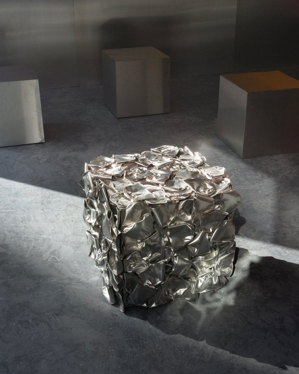 A closeup of a stainless steel stool covered in cast steel versions of crumpled coffee cups.