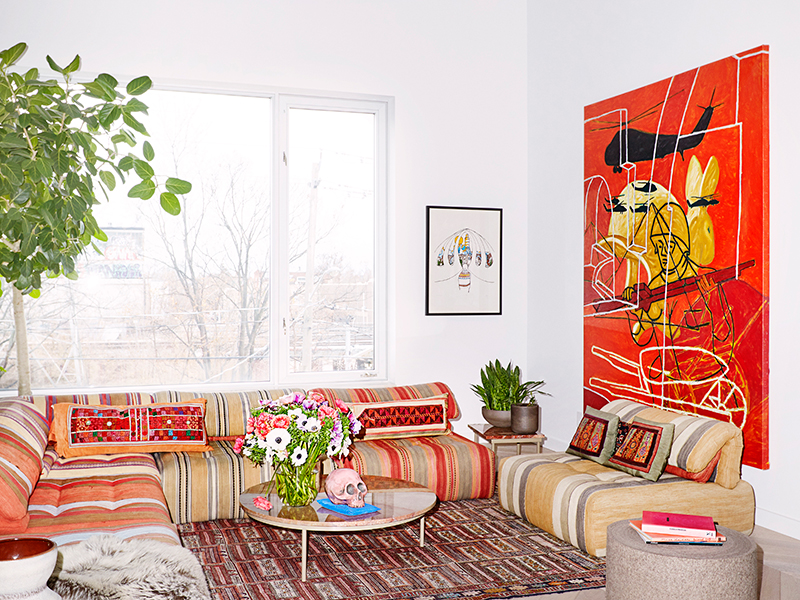 DesignTO Geary Avenue House - red and brown striped sofa, coffee table with flowers, white walls, and a red abstract painting