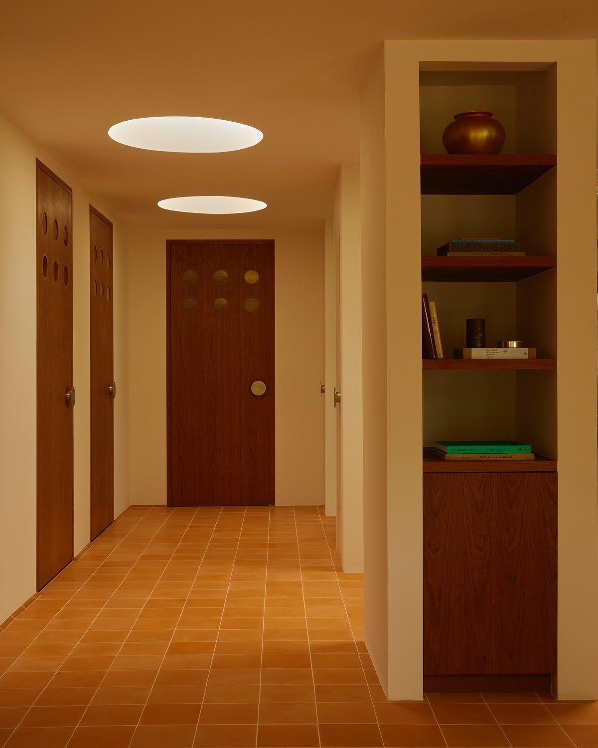 An office design by 22RE for LA creative agency Day Job features circular skylights and orange concrete tiles in a hallway with several wooden doors.