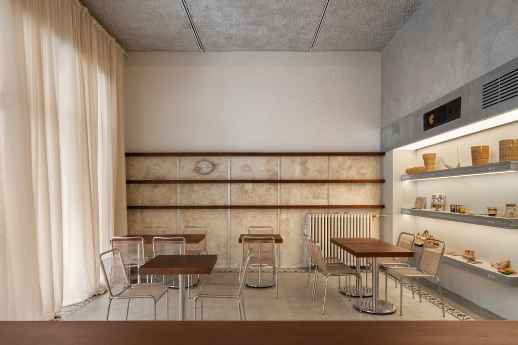 Stainless steel chairs sit clustered around wooden tables in a room with worn plaster walls.
