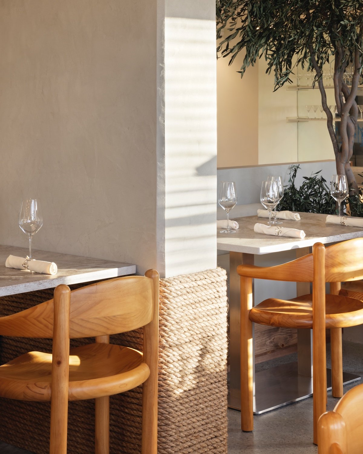 Rope wraps around a column in between two curved pinewood dining chairs inside Vancouver Greek restaurant Selene by design studio &Daughters.