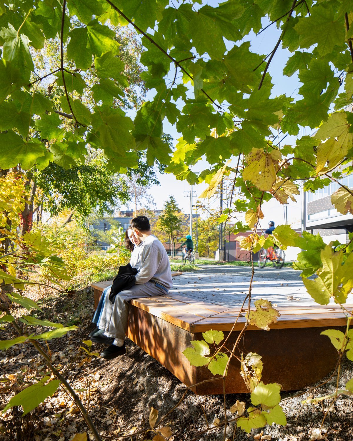 A couple sit at the edge of a wooden deck, hanging their legs over the edge looking out to a cluster of trees at Gorilla Park in Montreal.