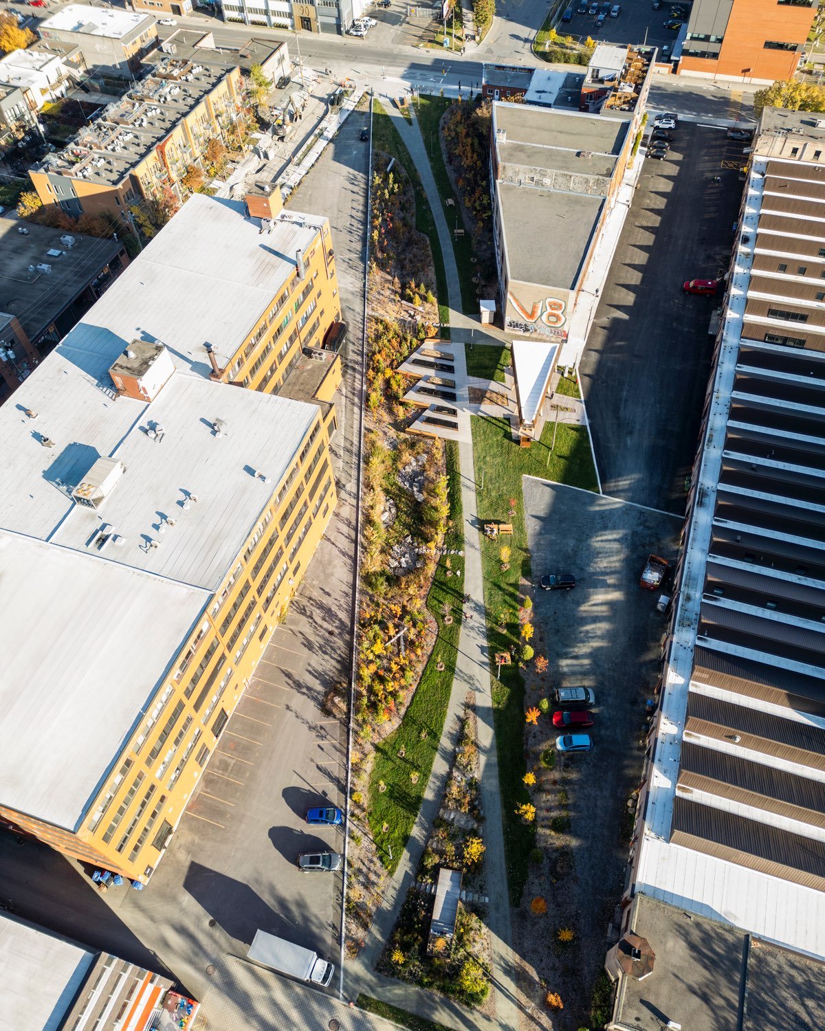 An aerial view of Gorilla Park in Montreal by urbanism design studio Civiliti, showing a paved curving path that crosses between clusters of forest to the left and a triangular pavilion to the right.