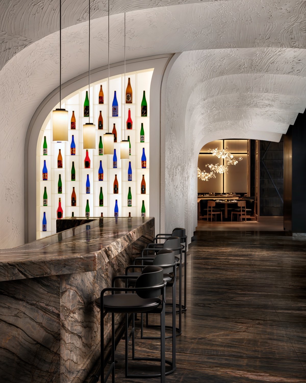 The sake bar at Nobu toronto featuring a glowing wall lined with bottles of sake and rippling panels on the ceiling that resemble a wave.