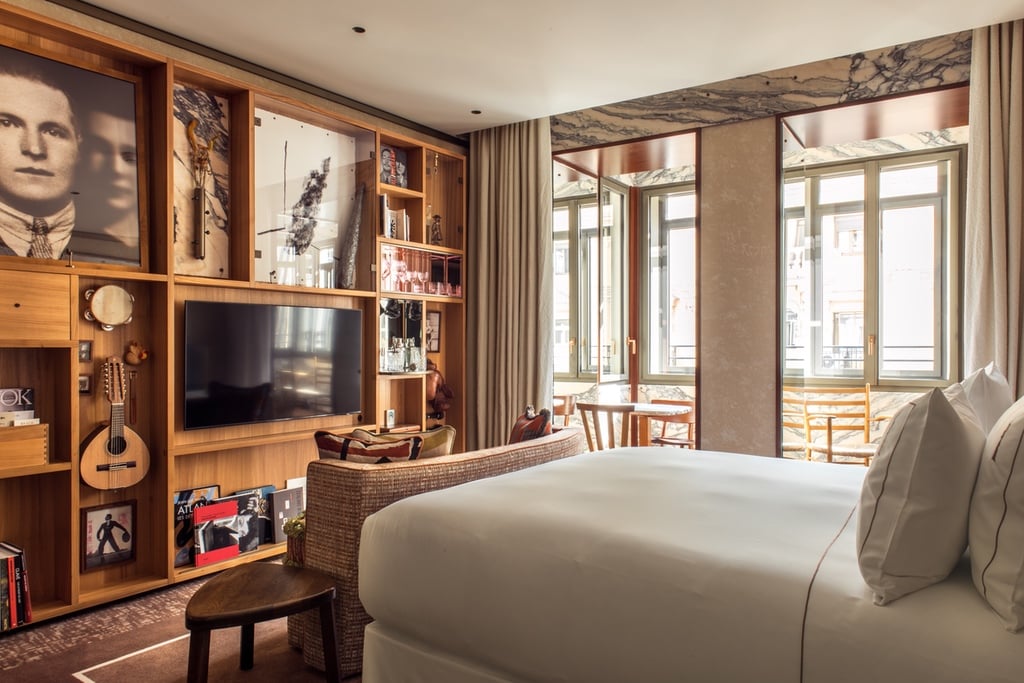 A bed in a guest room at the Brach Madrid hotel designed by Philippe Starck features a wall lined with wood cabinets that frame a portrait of a couple, a small banjo and many other decor items.