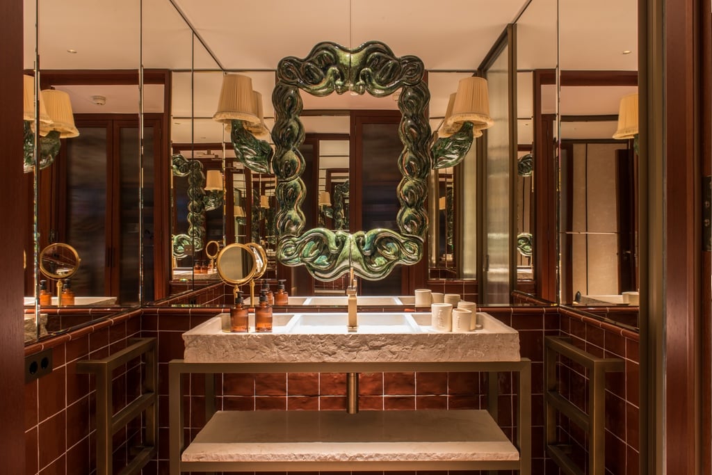 A sculptural green mirror with two lampshades extending out of it hangs in a mirrored bathroom at the Brach Madrid hotel designed by Philippe Starck.