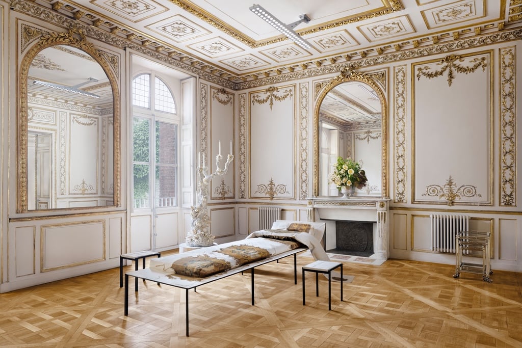 A modern daybed sits in an ornate, historic residential room with lots of gold trim and crown mouldings.