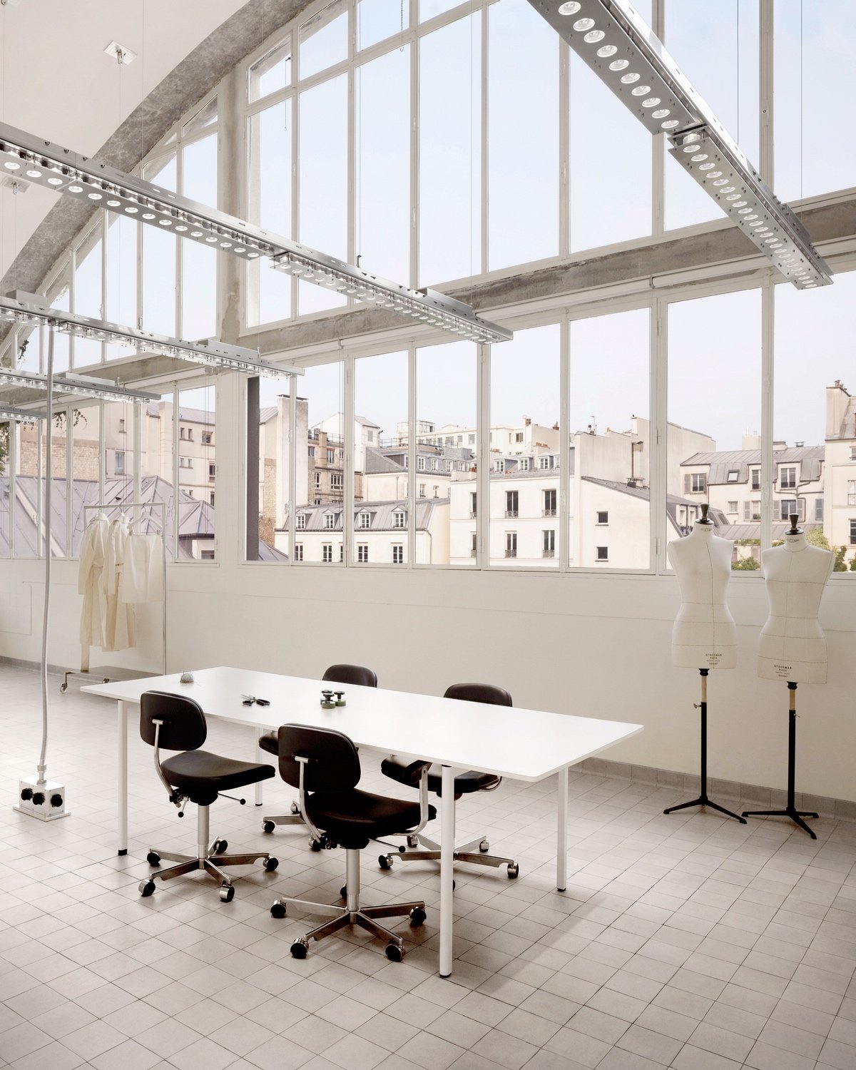 A view of four black chairs seated at a white table in the fashion studio at the Paris headquarters of Acne Studio designed by Halleroed and featuring a big rounded window.