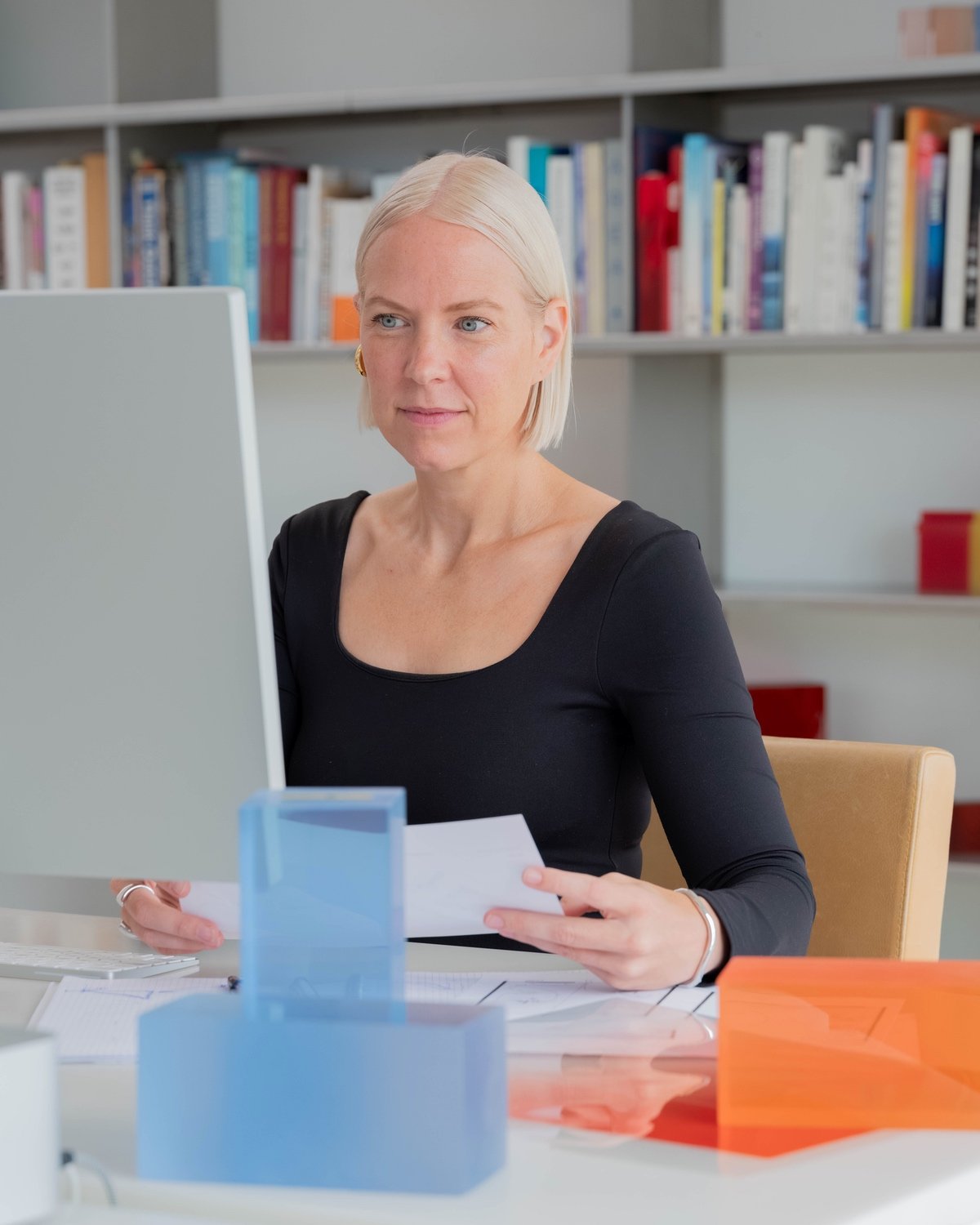 Dutch designer Sabine Marcelis seated at her computer screen with a series of blue and orange blocks next to it.
