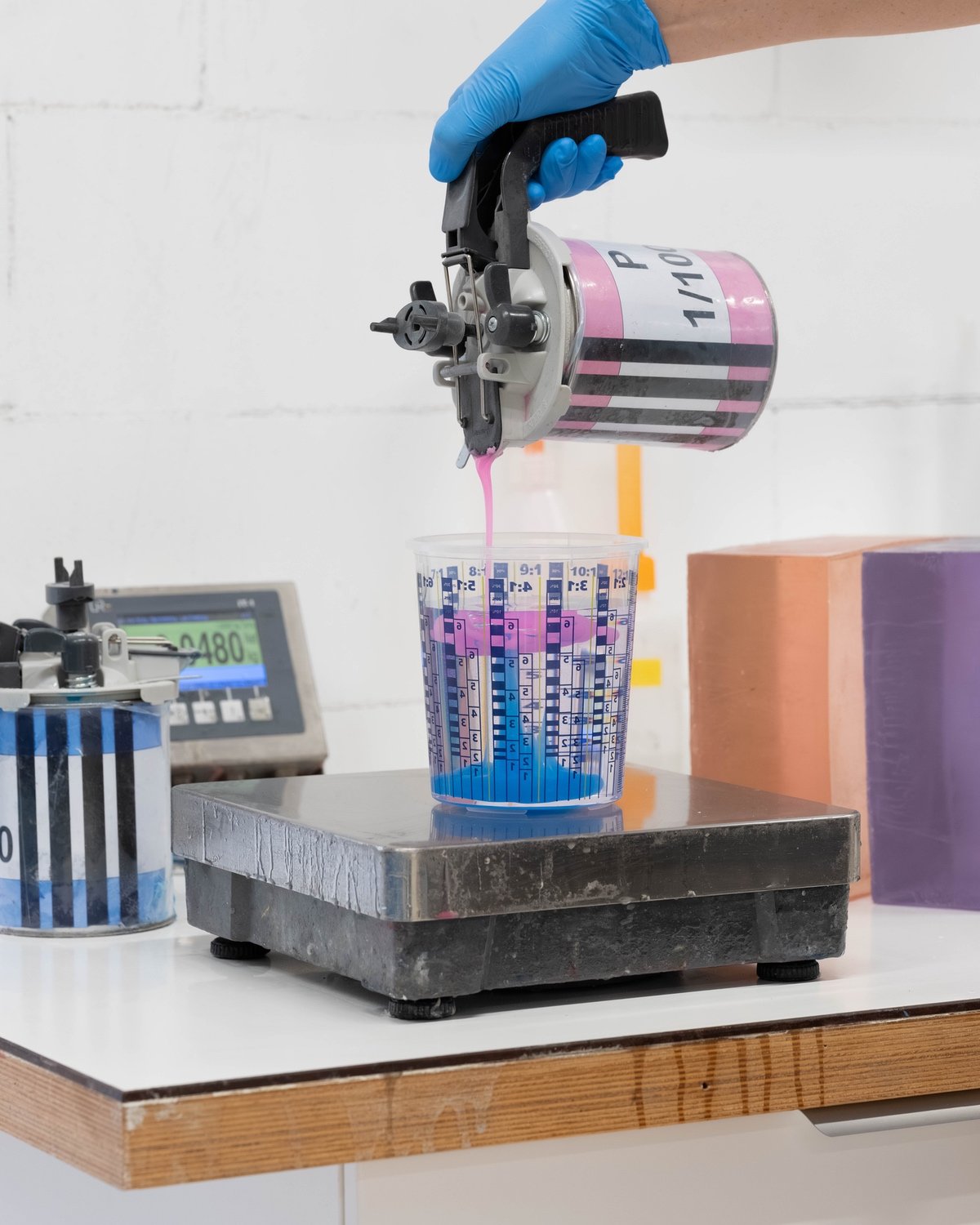 A hand wearing a blue glove pouring a blue substance into a measuring cup.