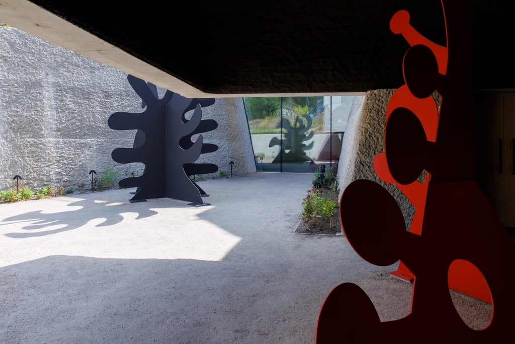 Two sculptures in a sunken concrete garden. The one on the left is black and the one on the right is red, and both have amoeba-like shapes.