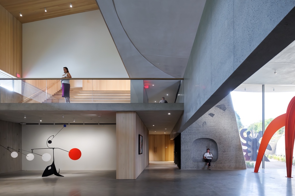 A gallery at Calder Gardens in Philadelphia, showing a woman on a balcony in a double-height room clad in concrete with sculptures on the ground floor.