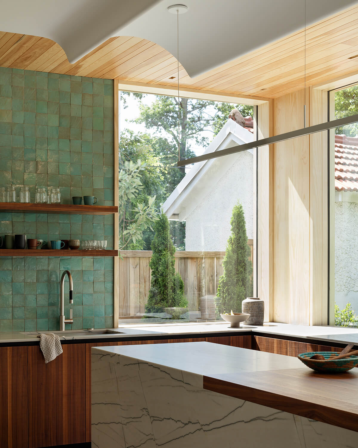 A mix of materials — warm pine ceiling planks, dramatic quartzite counters, rich walnut cabinets and hand-made tiles — creates a layered and inviting backdrop for busy family life.