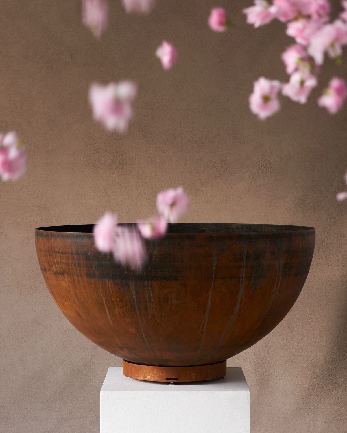 A deep Corten steel Été planter with pink petals falling around it.
