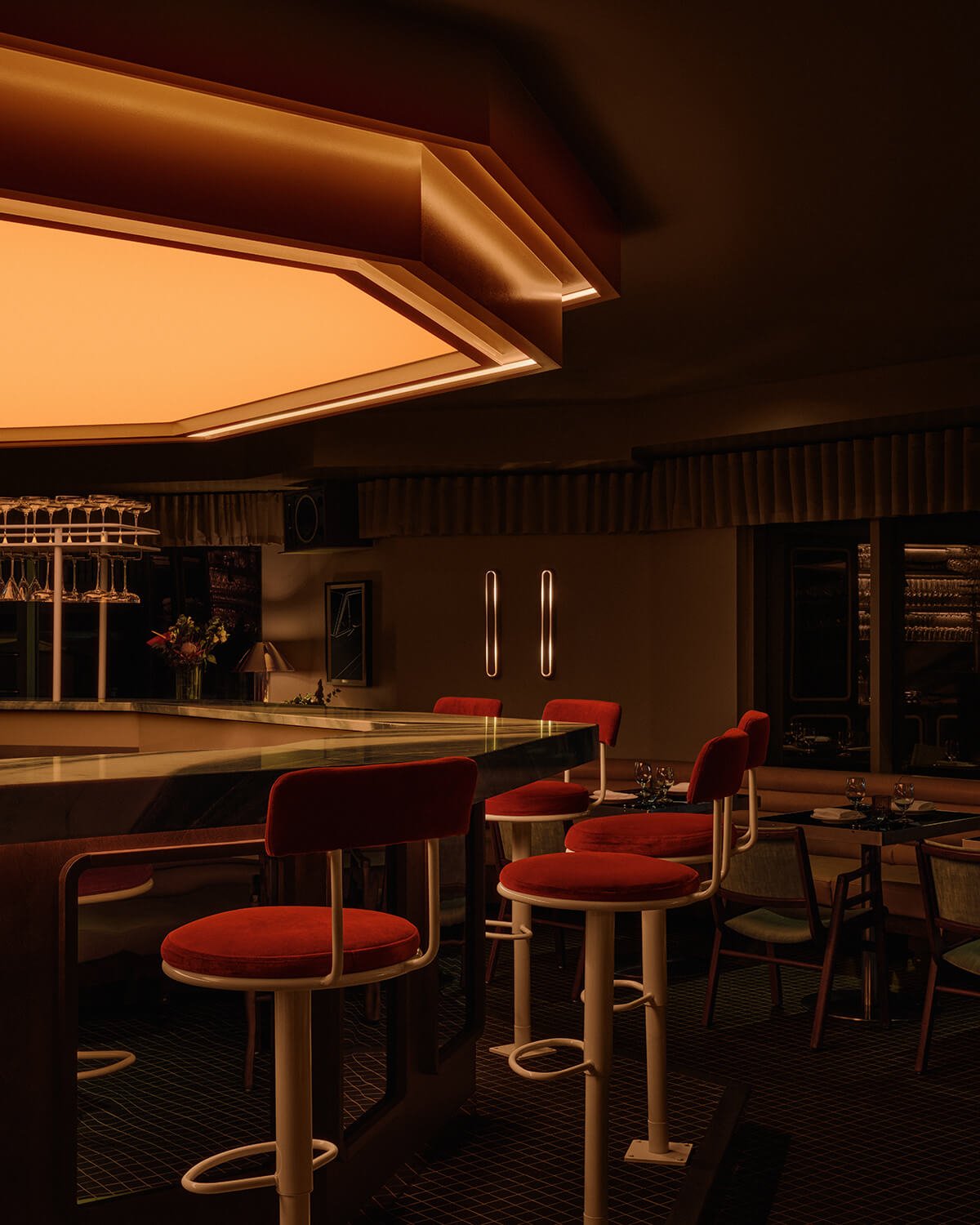 Bar with amber lightbox above and red velvet bar stools