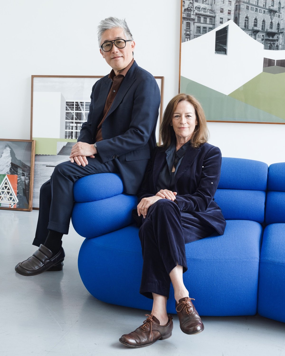Architects Mark Lee and Sharon Johnston in black suits sitting on a blue version of Knoll's Biboni sofa, which looks like a puffy Michelin Man.