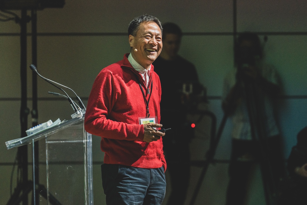 A portrait of landscape architect Kongjian Yu in a red sweater delivering a lecture onstage.