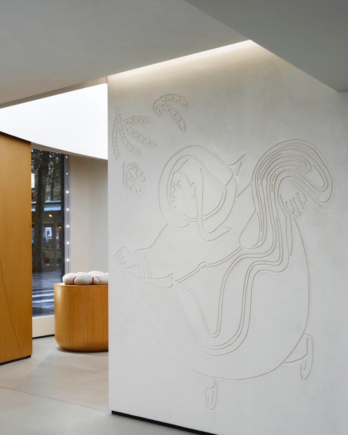 A wall featuring a carved illustration of an Inuit person wearing a traditional Amauti parka. To the left on a wooden podium is a sculpture recreating the stones of a fire pit.