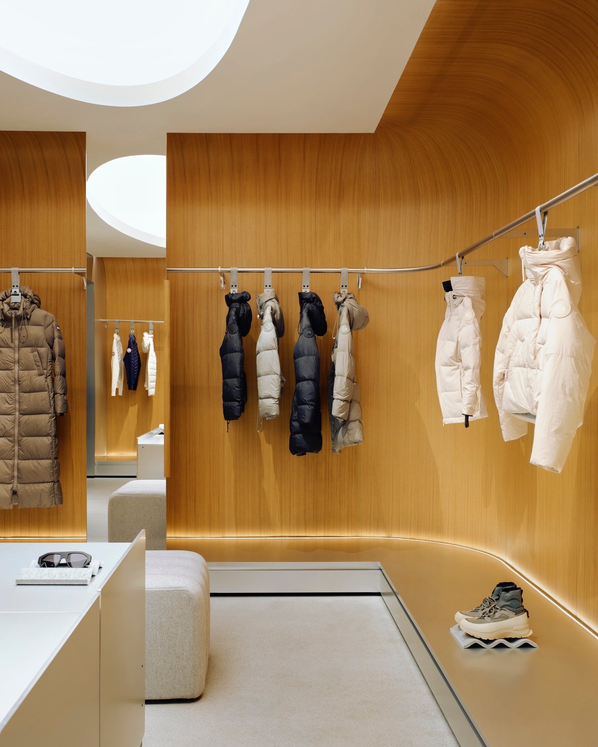 A selection of white and black winter coats on clothing racks hanging against an oak wall.