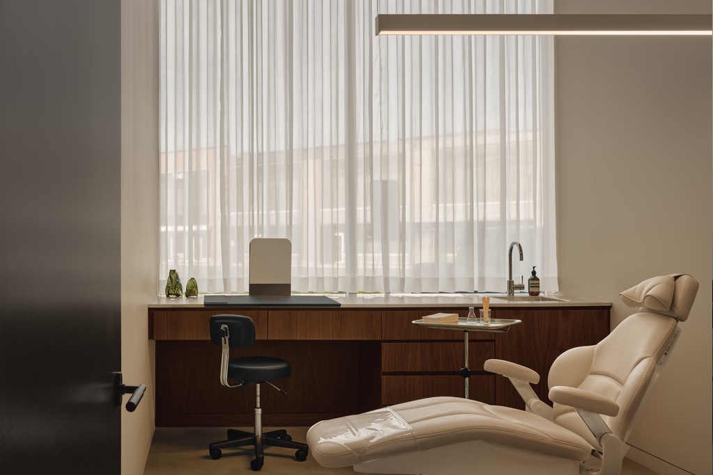 A medical treatment chair inside a clinic room with a wood-panelled desk.