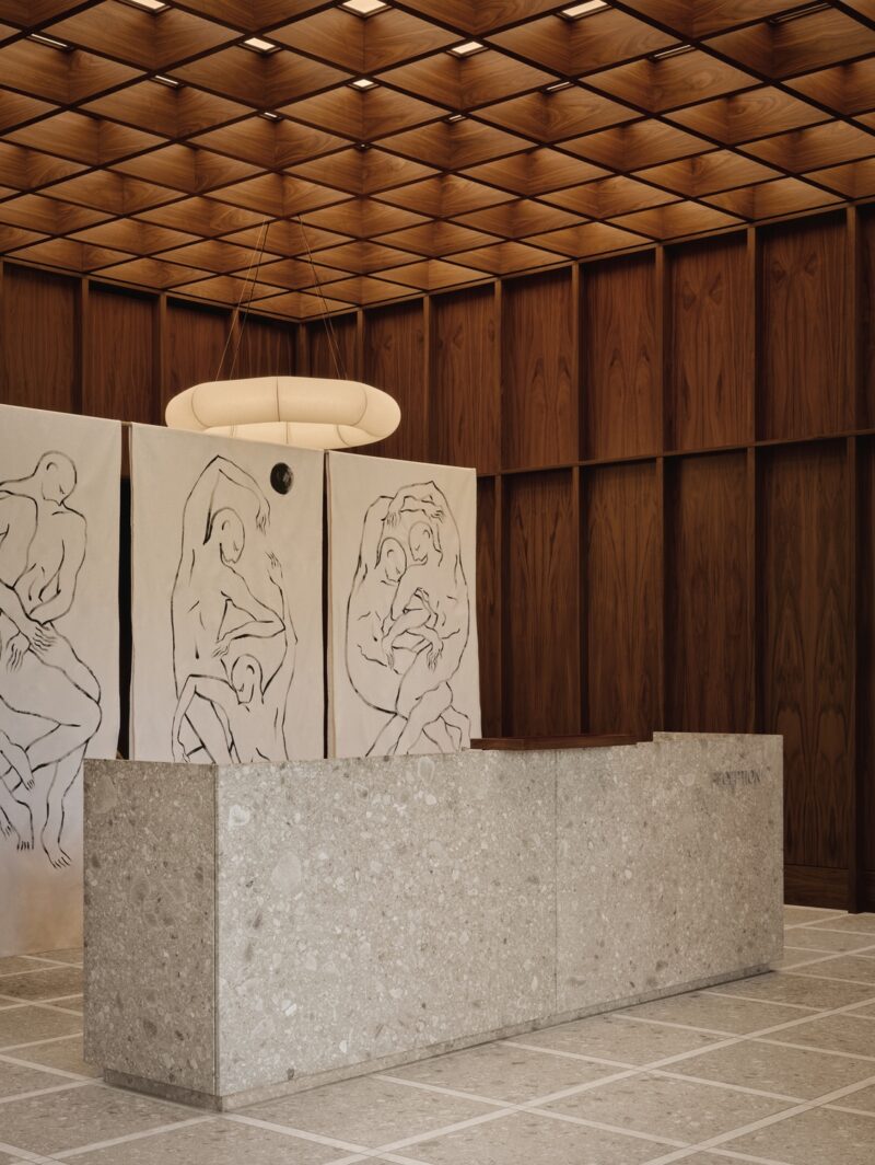 A stone reception desk sits in front of a divider screen decorated with illustrations of human bodies inside the double-height lobby of Surface Dermatology clinic in Oakville.