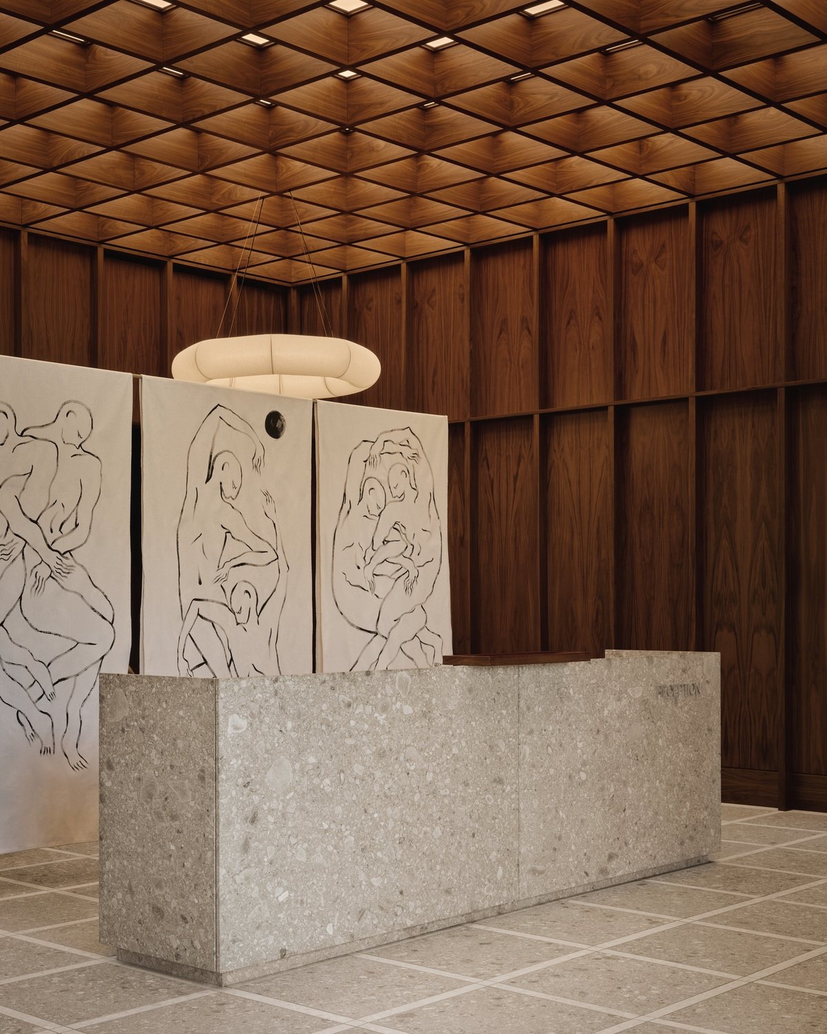 A stone reception desk sits in front of a divider screen decorated with illustrations of human bodies inside the double-height lobby of Surface Dermatology clinic in Oakville.