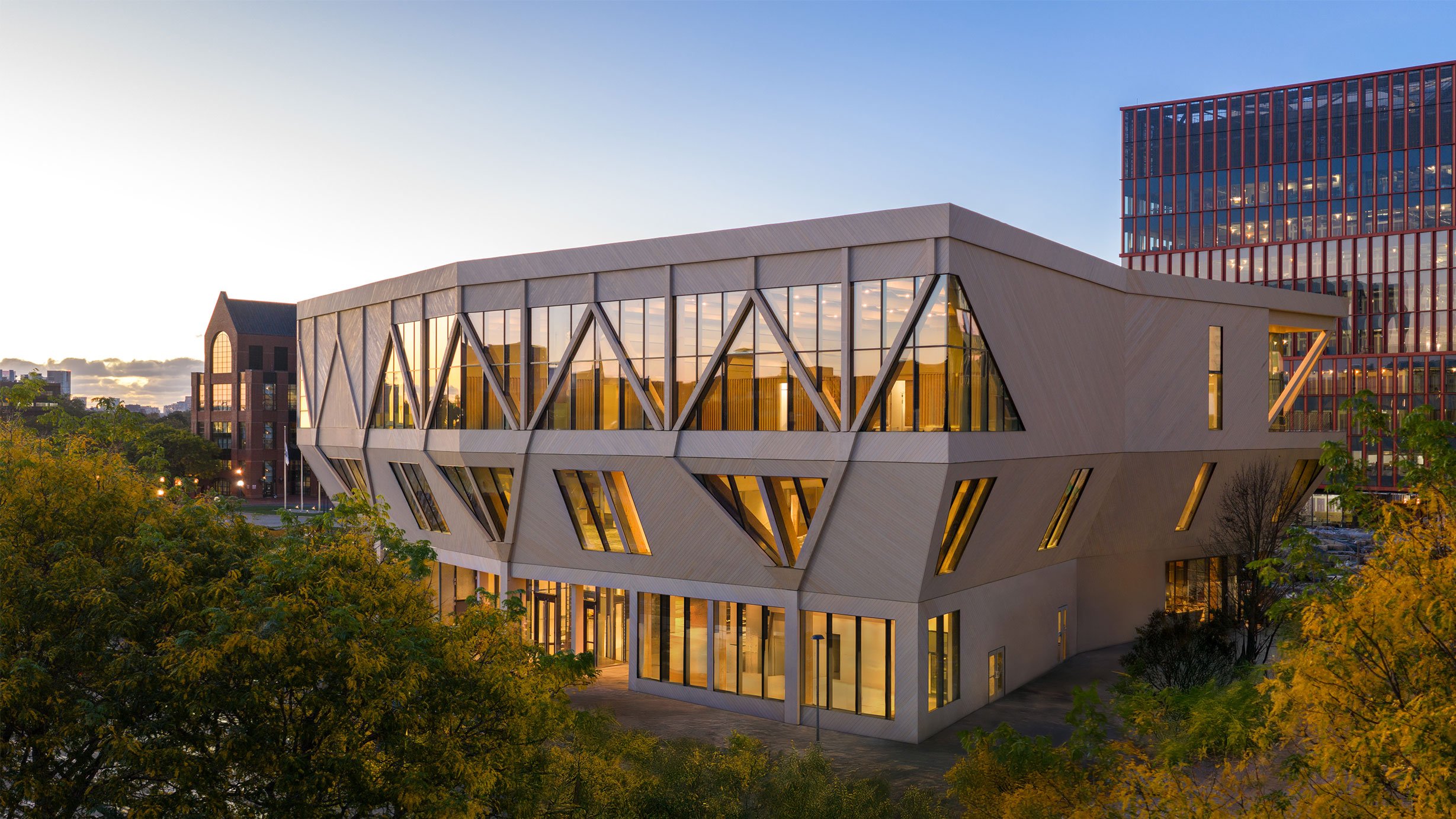 The Harvard Rubenstein Treehouse, one of the best buildings and top architecture projects of 2025, at dusk with a wood-clad exterior and angular columns supporting the cantilevered top floor with large glass windows.