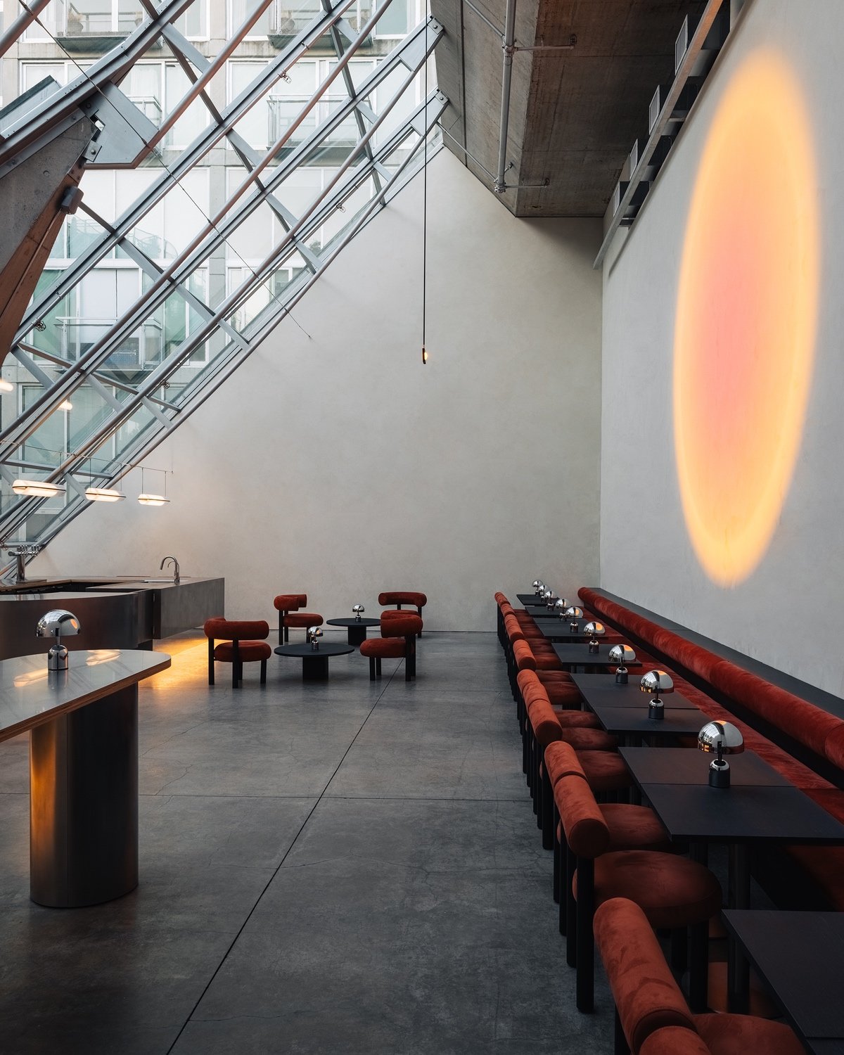 A row of red velvet chairs sit against the back wall opposite a sloped glass wall at Ellipsis Vancouver.