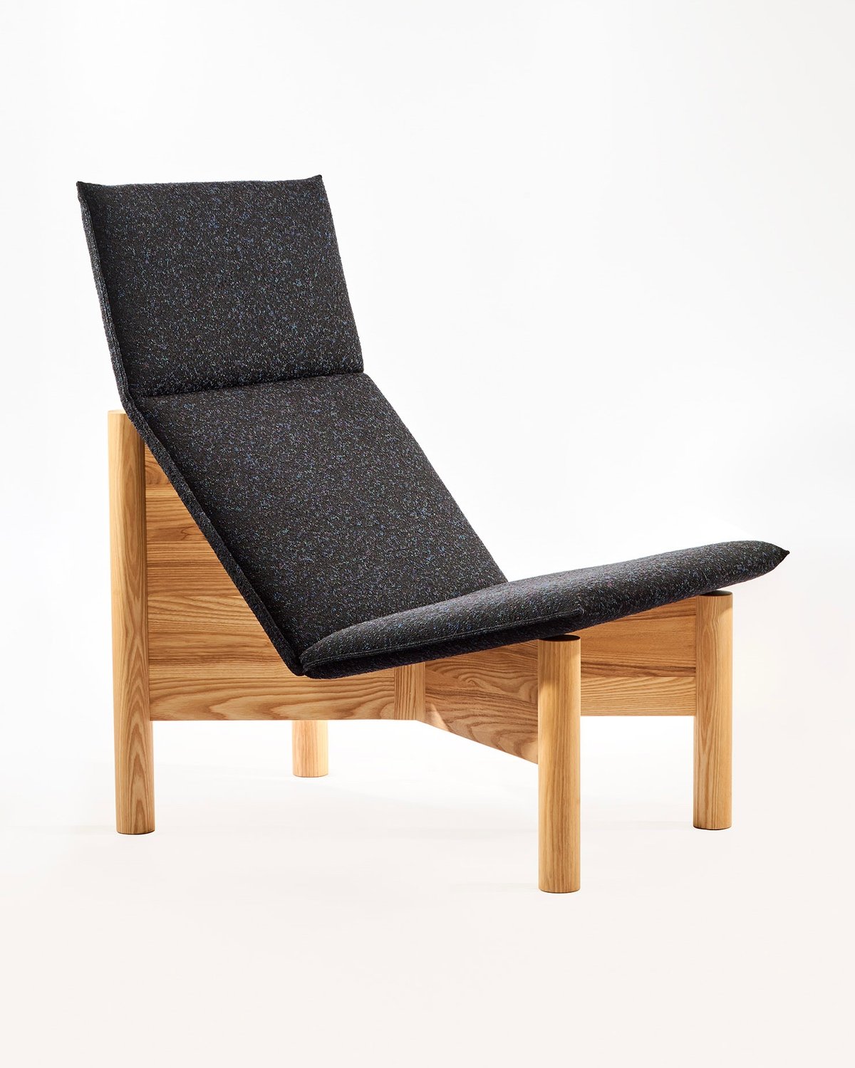 A wood lounge chair with an upholstered cushion designed by Them Fougere for the modern Canadian furniture brand Ourse.