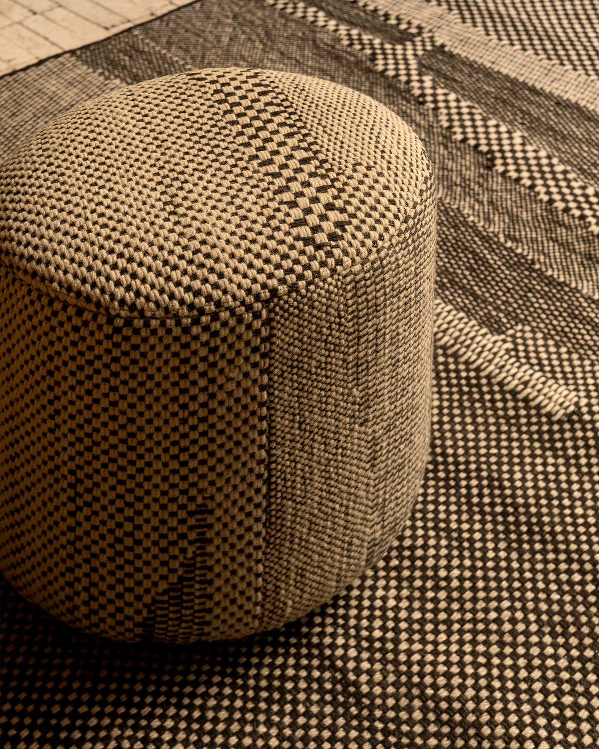 A closeup of the knitted pattern on a small pouffe sitting on top of a matching rug.