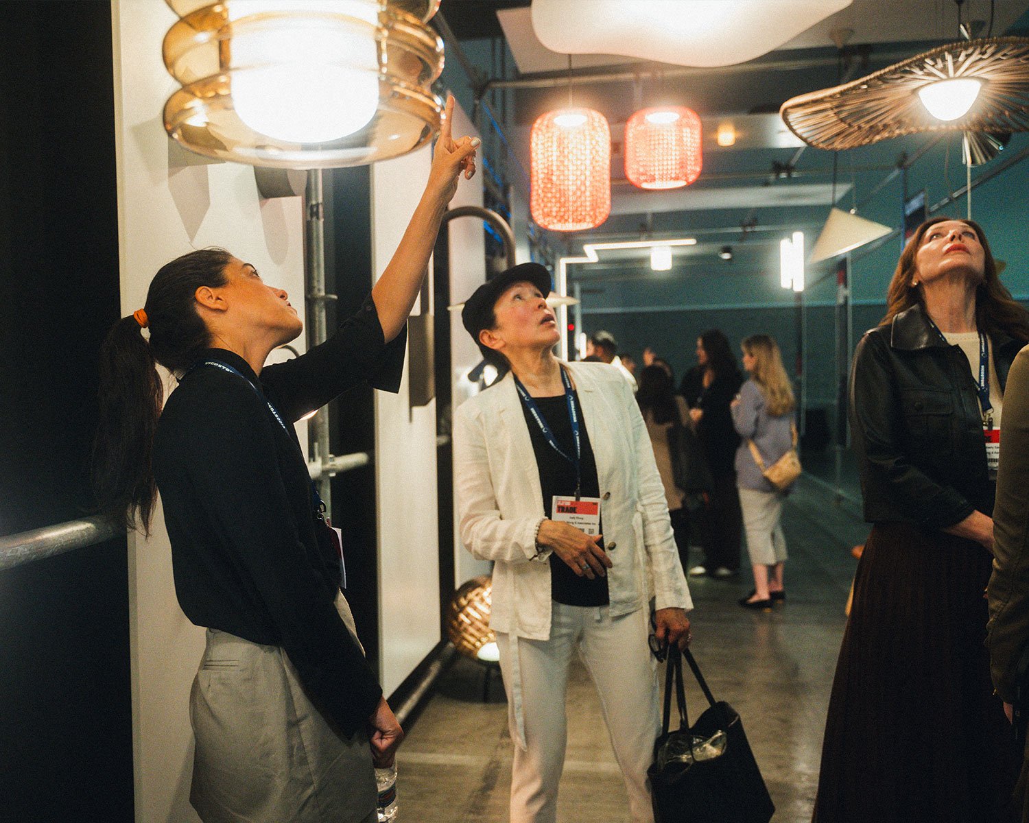 Three women stand underneath a series of glowing pendant lights as part of a trade show lighting display that will be featured at IDS Toronto 2026.