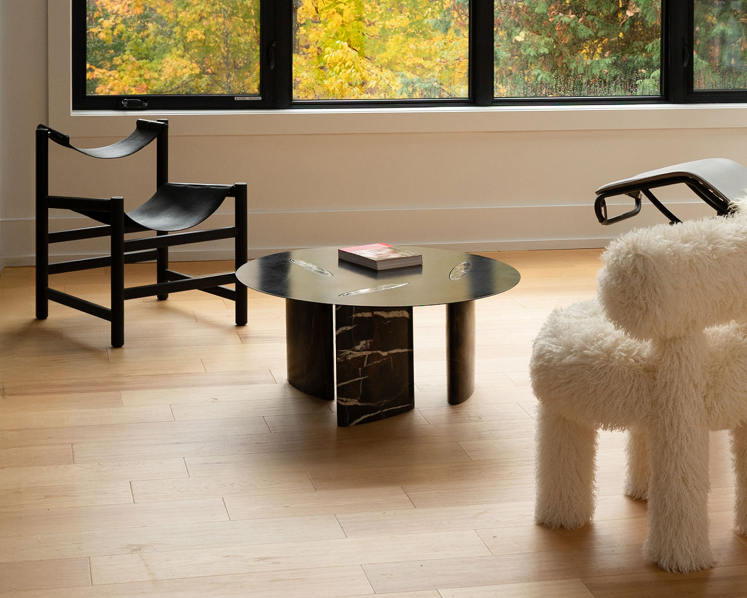 A black sling chair sits on one side of a circular coffee table, with a furry white lounge chair on the other.